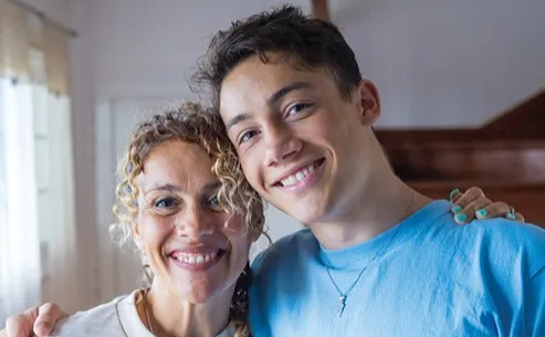 Mother and son smiling with one arm around each other's shoulders.