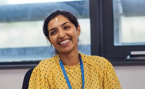 Woman wearing bright yellow polka dot blouse and blue lanyard smiling