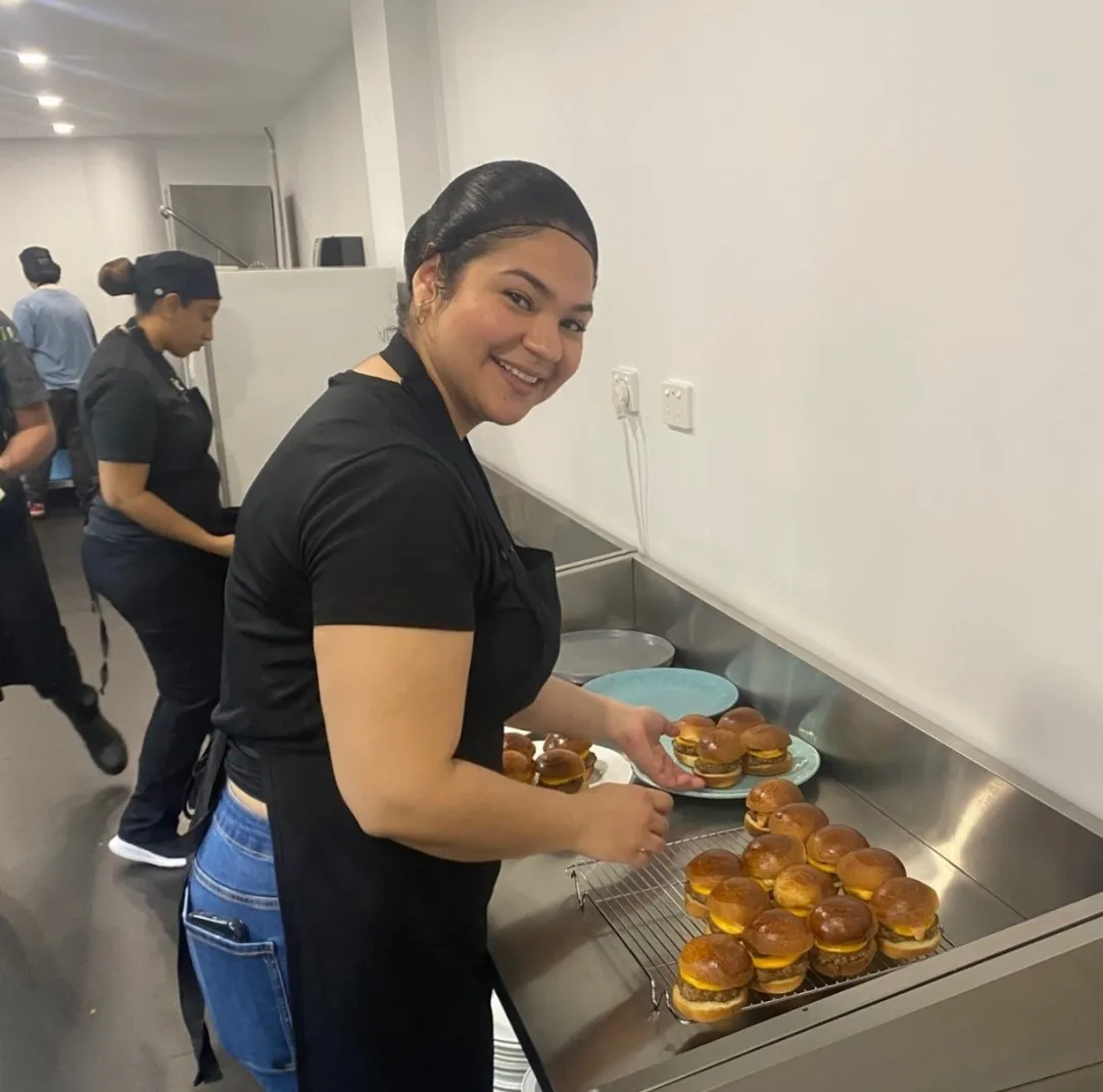 Chef assembling sliders in a kitchen wearing apron and hair net