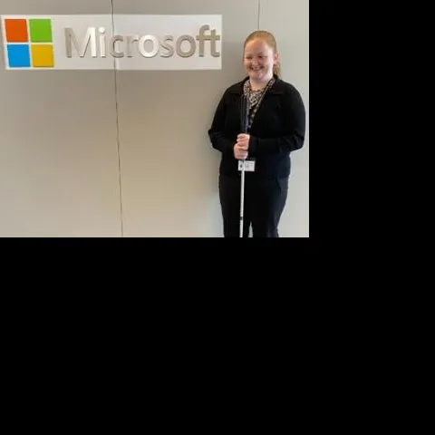 Person wearing block clothes and lanyard standing next to Microsoft logo