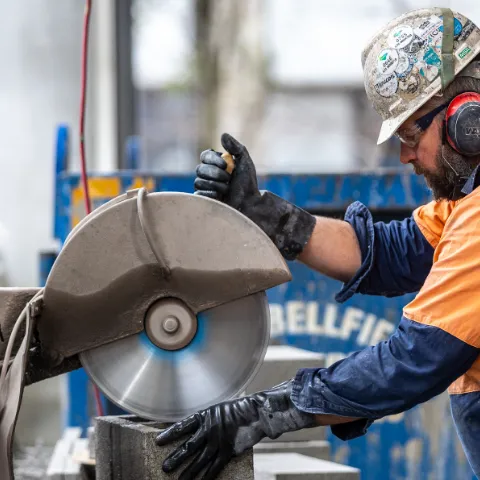 Worker wearing PPE while using a buzz saw on a piece of metal