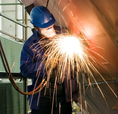 Worker wearing PPE holding welding tool with sparks flying
