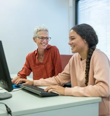 Two people sitting at a desk typing on keyboards while they are smiling.