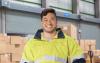 Warehouse worker wearing yellow hi vis work jacket surrounded by boxes while standing in warehouse