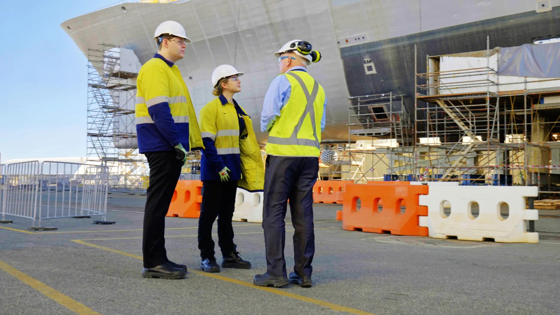 mentor mentoring apprentice trainee programs we are recruiting for ship work dock ship building young apprentice or trainee talking with mentor in front of ship construction blue-collar worker building clothing construction worker engineer hard hat high-visibility clothing outdoor person sky standing workwear