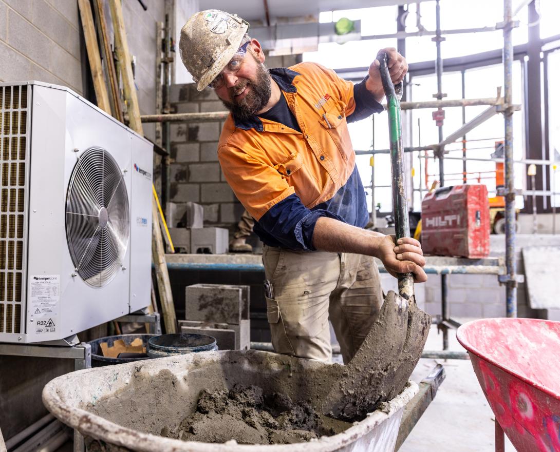 Employers ADMS construction working mixing cement or mortar with a shovel in a wheelbarrow smiling hard hat high vis construction site indoors blue-collar worker building clothing footwear man person