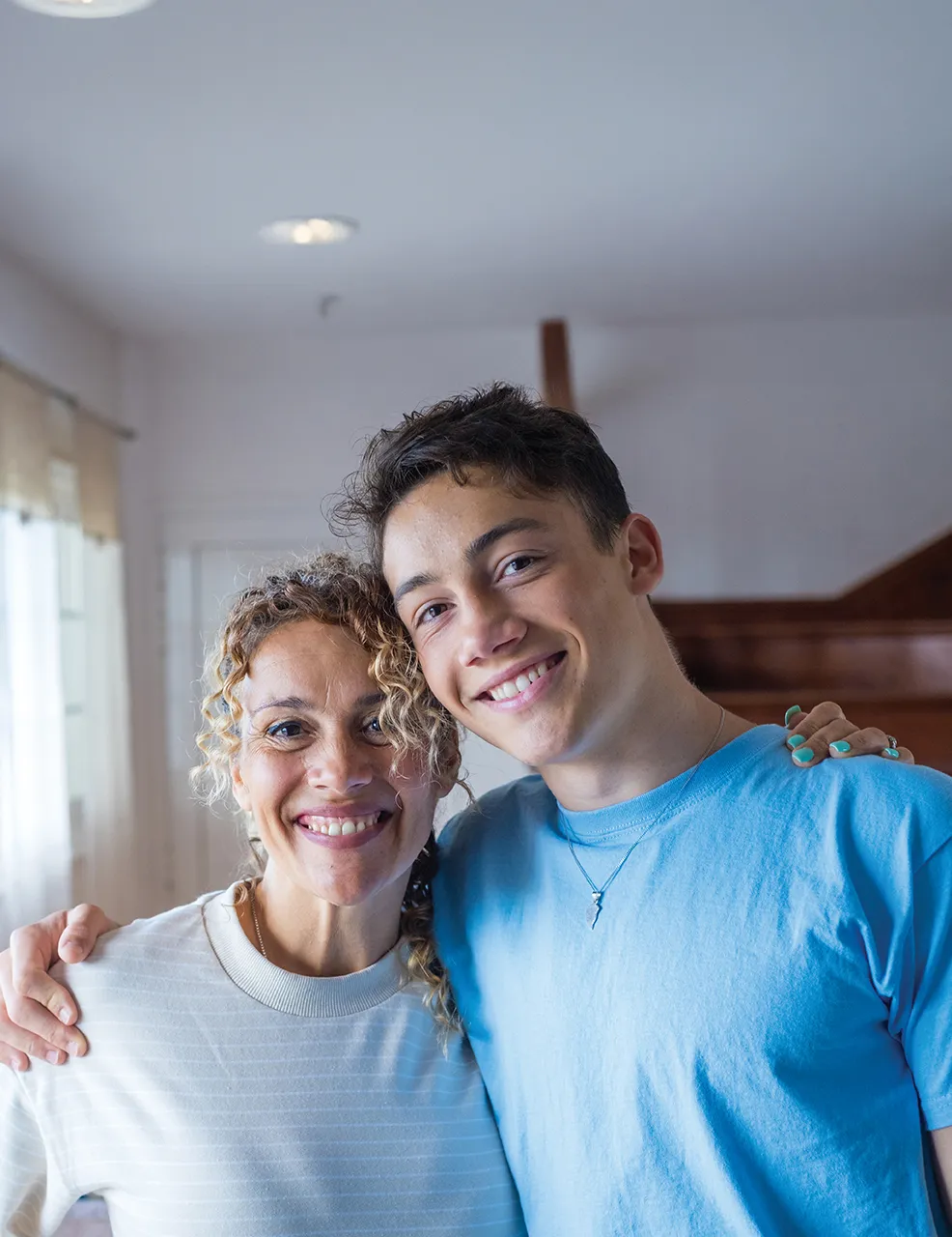 Mother and son smiling with one arm around each other's shoulders.