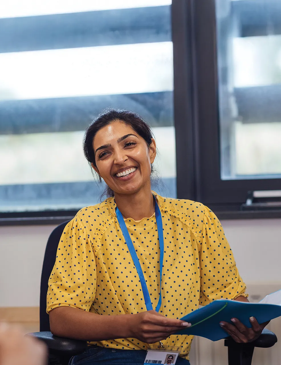 Woman wearing bright yellow polka dot blouse and blue lanyard smiling