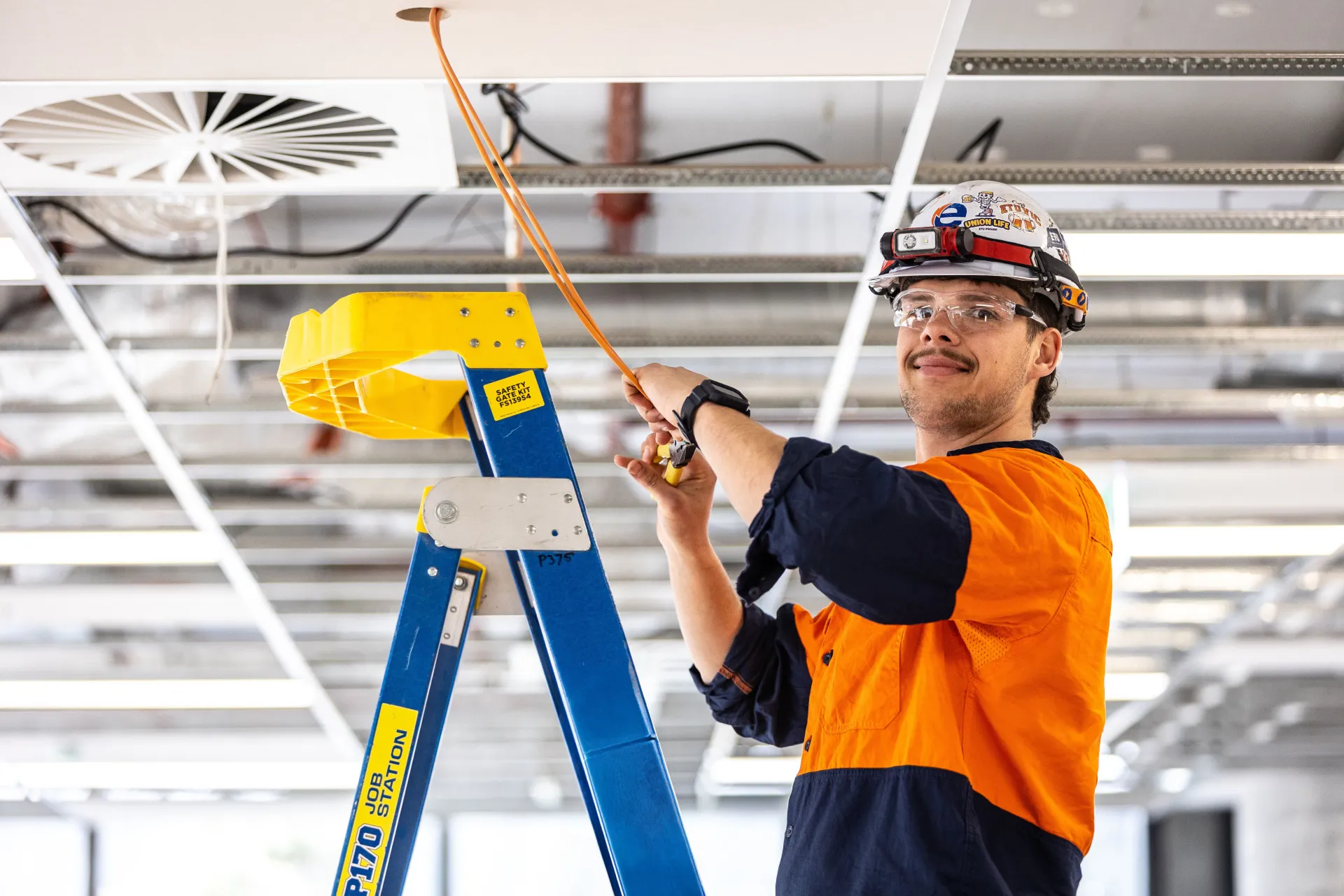 Electrician standing on ladder working on electricals inside a ceiling