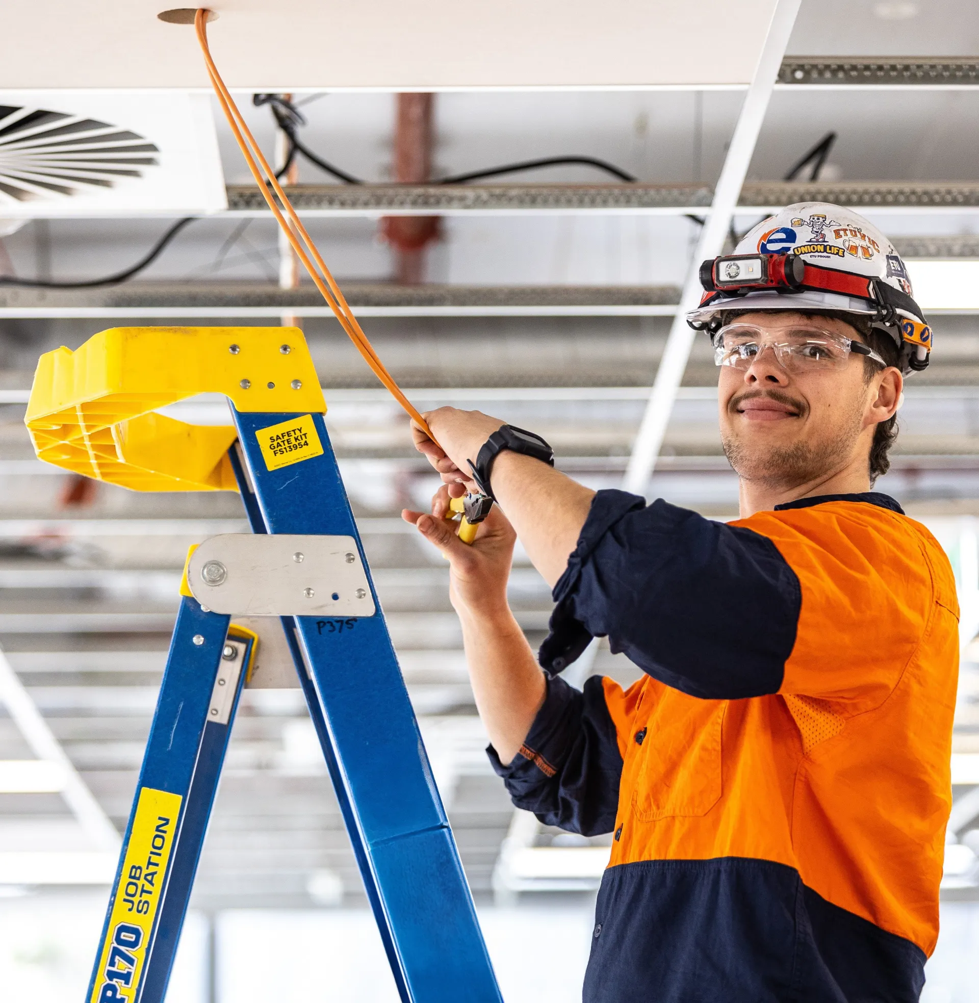 Electrician standing on ladder working on electricals inside a ceiling